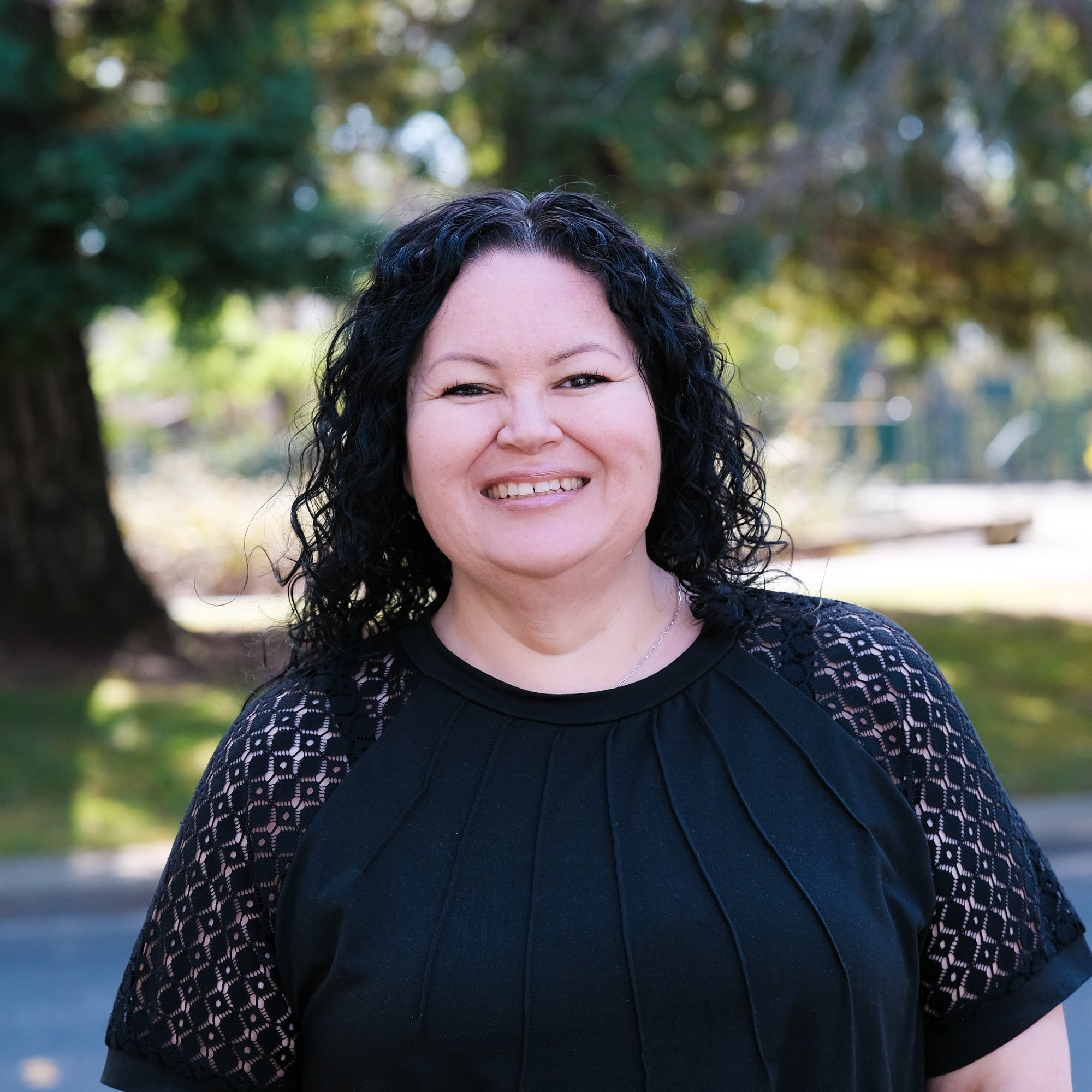 a person smiling in front of some trees 